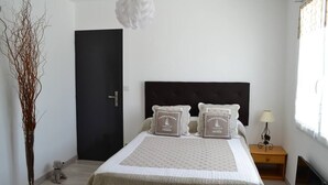 Un dormitorio con cama, una puerta negra, una mesita de noche con lámpara y una ventana con cortinas.