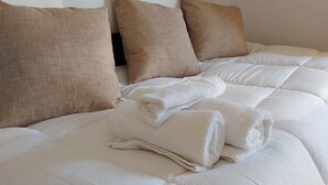 A neatly made bed with white bedding and three beige pillows. - Bluegonia. (Έξω Γωνιά)