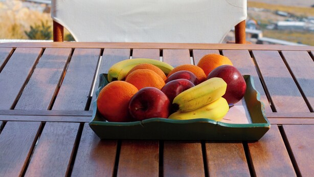 A table with a fruit tray and a view of the ocean. - Bluegonia. (Έξω Γωνιά)
