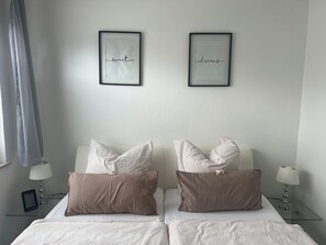 A hotel room with two beds, each with striped bedding and pillows, a bedside table with a lamp, and two framed pictures on the wall.
