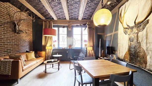A cozy room with a brick wall, a wooden ceiling, a wooden dining table, and a sofa.