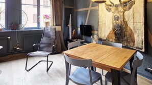 A dining area with a wooden table and chairs, a large painting of a deer on the wall, and a window with curtains.