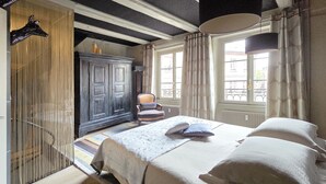 A bedroom with a bed, a chair, a wardrobe, and a window with curtains.