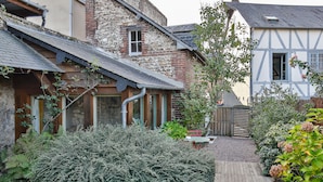 A traditional half-timbered house with a stone facade, wooden beams, and a small garden area with shrubs and a wooden bench. - Le Cottage de La Maison Saint Léonard | Lovely Shared Garden in the Heart o (Honfleur)