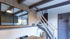 A dining area with a wooden table and chairs, a large mirror, and a staircase leading to another level. - Le Cottage de La Maison Saint Léonard | Lovely Shared Garden in the Heart o (Honfleur)