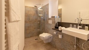 Een moderne badkamer met een douchecabine van glas, een wit toilet en een grote spiegel boven een witte wastafel.