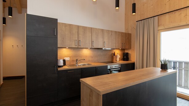 Een moderne keuken met donkere kastjes, een houten aanrechtblad en hanglampen.