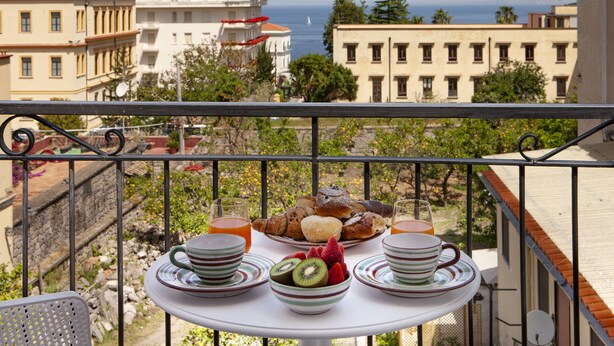 Un balcón con una mesa dispuesta para el desayuno, con vistas a la ciudad y al mar.