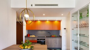 Una cocina moderna con una mesa de madera, un tazón de fruta y un armario de vidrio con vajilla.