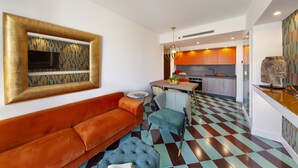 Una sala de estar moderna con un sofá, un reposapiés y una pared estampada. Se ve un área de cocina al fondo, con una mesa de comedor y sillas.