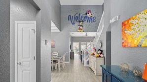 A hallway with a 'Welcome' sign, a dining area, and a staircase leading to another level.