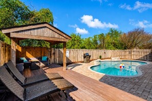 Un jardin avec une terrasse en bois, un espace salon couvert et une piscine.