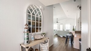 Uma sala de estar ampla, com pé direito alto, uma grande janela em arco e um console de madeira com objetos decorativos.