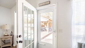 Uma porta branca com painel de vidro jateado e painel de vidro transparente, uma mesinha com abajur, e uma placa acima da porta.