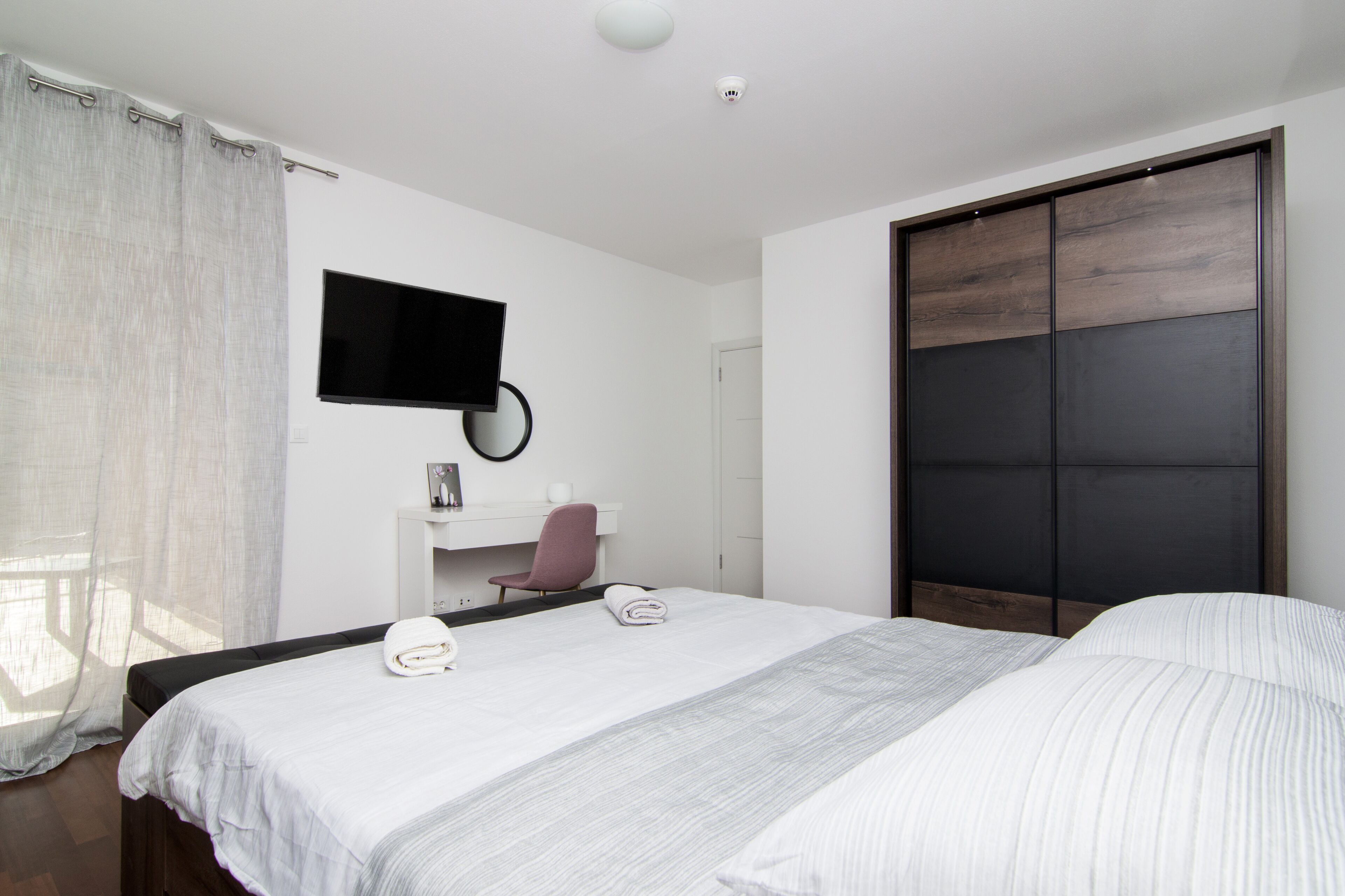 A hotel room with a bed, a desk, a chair, a television, and a wardrobe.