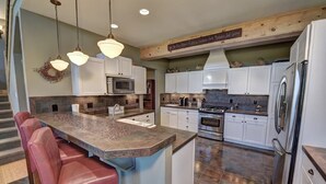 Una cocina amplia con una isla central, muebles blancos, electrodomésticos de acero inoxidable y techo de madera.