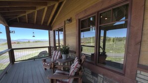 Una terraza de madera con una mesa y sillas, ventanas grandes y vistas al paisaje.