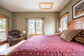 A bedroom with a large bed, a leather chair, a window with curtains, and a wooden headboard.
