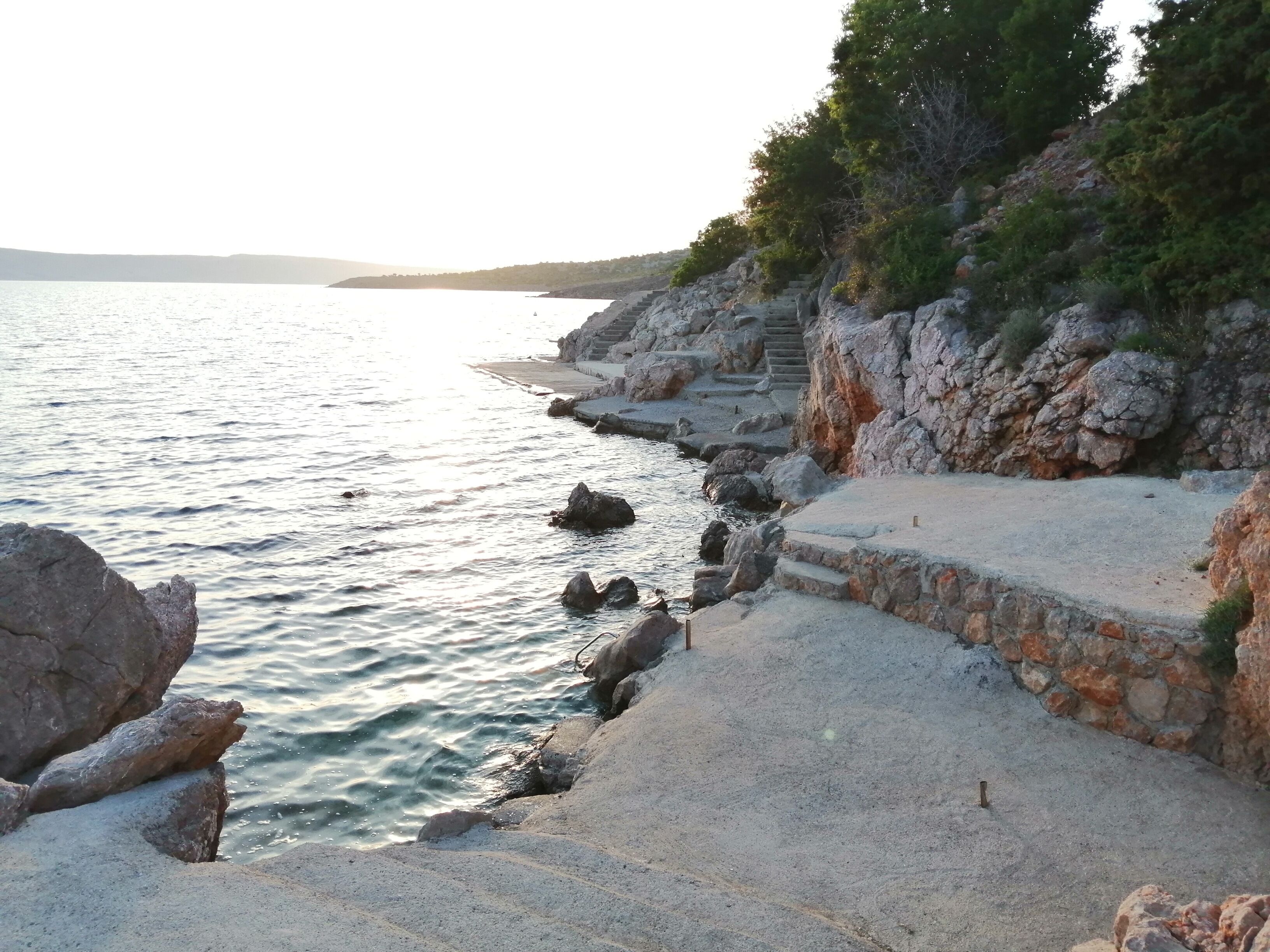 A coastal area with a stone staircase leading down to the water, surrounded by rocky terrain and sparse vegetation.