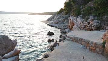 A coastal area with a stone staircase leading down to the water, surrounded by rocky terrain and sparse vegetation.