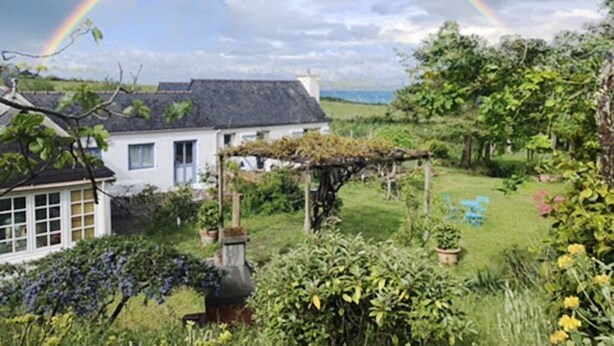 Ein Haus mit Garten, einem Regenbogen und einem Berg im Hintergrund.