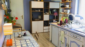 Eine kleine Küche mit Esstisch, Stühlen sowie verschiedenen Küchengeräten und Utensilien auf Regalen.