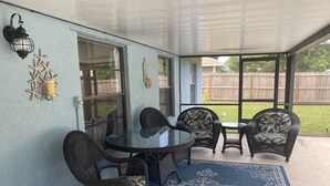 Une terrasse couverte avec une table en verre, des chaises en osier et un tapis à motifs bleus.
