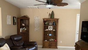 Un salon avec un canapé en cuir marron, un meuble en bois, un ventilateur de plafond et un tapis à motifs.