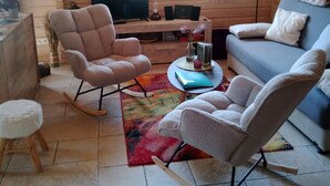 A cozy living room with a sofa, two rocking chairs, a TV, and a wooden interior. - Blockbohlenhaus "steiner Lodge" (Steinen)