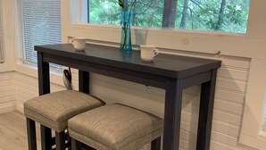 A dark wooden table with two cushioned stools, a vase with flowers, and a white mug on the windowsill. - Welcome to Our Little Slice of Heaven on the Lake! (Lake Lure)