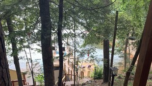 A wooden staircase leading to a deck area surrounded by trees, with a view of a body of water in the background. - Welcome to Our Little Slice of Heaven on the Lake! (Lake Lure)