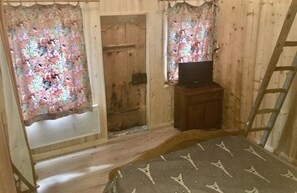 A room with wooden walls, a bed with a patterned bedspread, a television on a wooden stand, and a ladder leaning against the wall. - Chalet Savoyard (Jarrier)