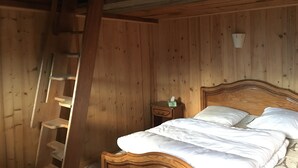 Puinen huone, jossa on sänky, yöpöytä ja puinen tikapuu.