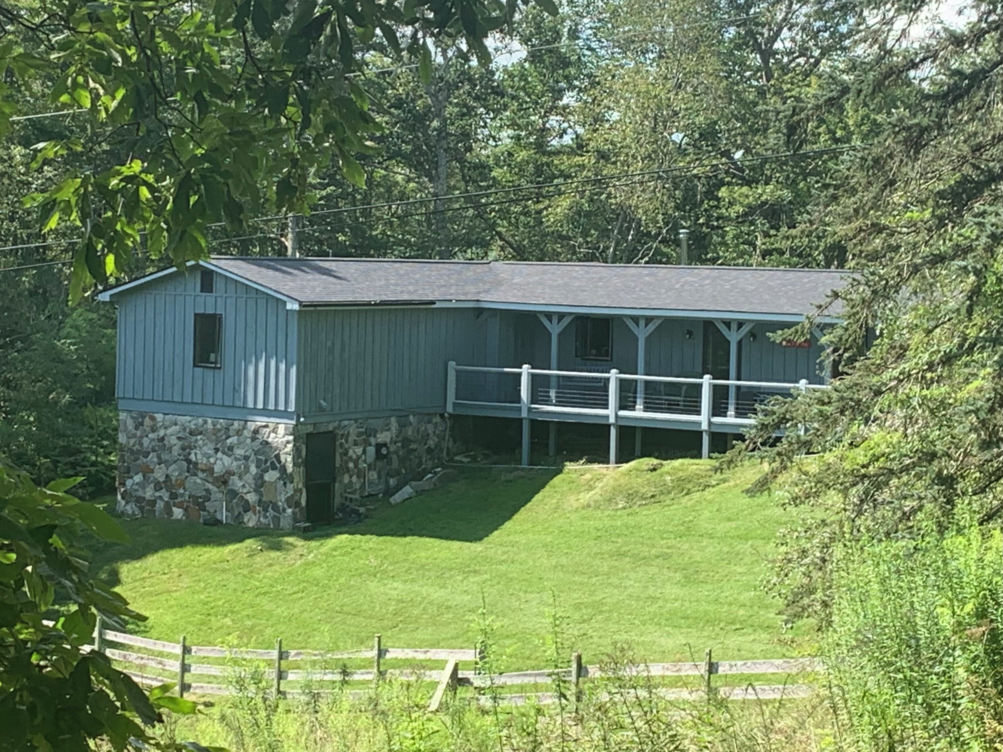 A single-story building with a stone foundation and a blue exterior, featuring a covered porch and a fenced yard.