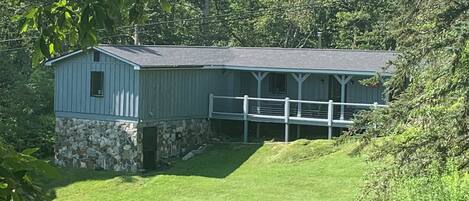 A single-story building with a stone foundation and a blue exterior, featuring a covered porch and a fenced yard.