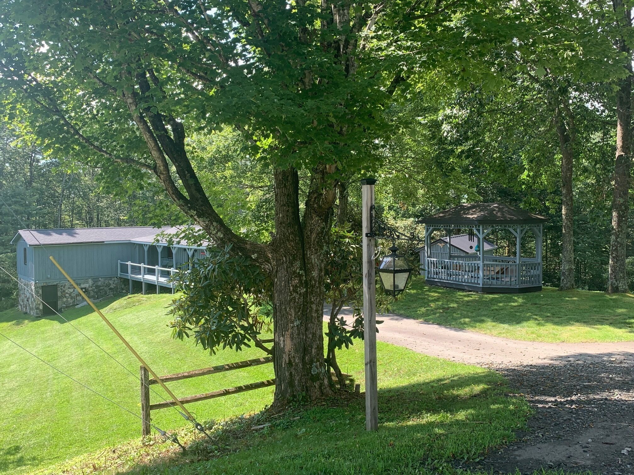 A gazebo, a covered structure with a roof, surrounded by a grassy area and trees.