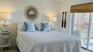 Quarto com cama grande, duas mesas de cabeceira com luminárias, espelho decorativo e dois remo de madeira na parede.