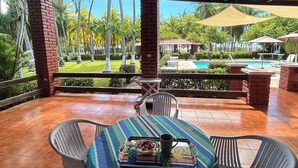 Une terrasse extérieure avec une table dressée pour deux personnes, entourée de chaises, donnant sur une piscine et des palmiers.