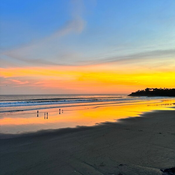 A beach at sunset with calm waves and a clear sky.