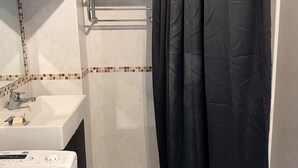 Ein Badezimmer mit einem weißen Waschbecken, einem Spiegel, einem schwarzen Duschvorhang und einer weißen Waschmaschine.