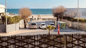 Eine Küstenstraße mit geparkten Autos, ein Strand im Hintergrund und ein klarer Himmel.