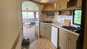 Cocina compacta para vehículos recreativos, con estufa a gas, pileta y armarios de madera.