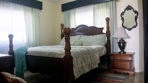 A bedroom with a four-poster bed, a nightstand with a lamp, and a mirror on the wall.