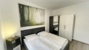 Una habitación de hotel con una cama, una mesita de noche, un armario y un cuadro de un bosque.