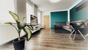 Una sala de estar moderna con una planta grande en maceta, un televisor de pantalla plana, una pared de acento color aguamarina, un sofá de cuero oscuro y una mesa de centro de madera.