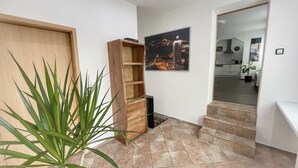 Un pasillo con puerta de madera, una planta, estantería de madera y suelo de baldosas.