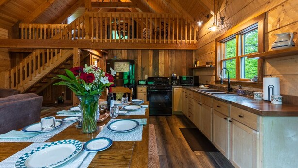 Interior de una cabaña de madera con comedor, cocina y dormitorio en entrepiso.