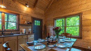 Cocina de cabaña de madera con una mesa de comedor para cuatro, un lavaplatos y una ventana con vistas a la vegetación.