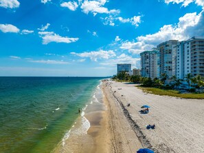 A beach with a row of high-rise buildings, clear blue sky, and calm sea.