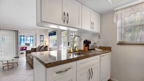 A modern kitchen with white cabinetry, a granite countertop, and a built-in dishwasher. - Apt#1-Charming relaxing -beautiful APT-80yard walk to the BEACH wBBQ/ Patio (Pompano Beach)